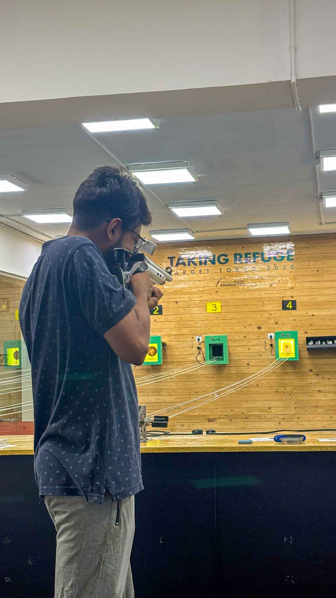 Close-up of a man aiming a rifle at an indoor shooting range with wooden target boards in Bengaluru.